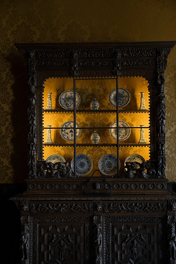 Vintage china display of blue and white chinoiserie plates and vases in a carved wood cabinet with glass doors, softly backlit inside