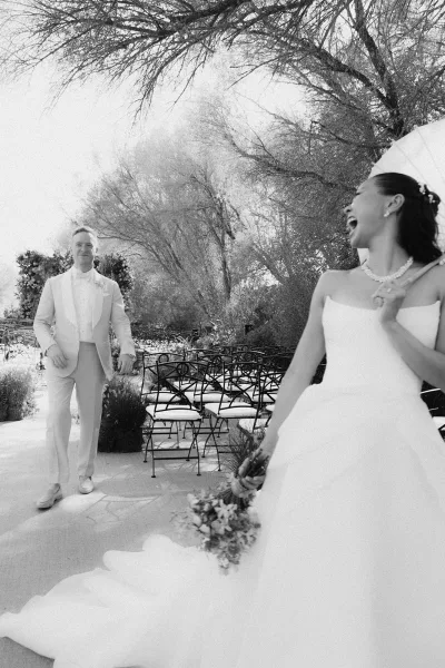 Couple portrait capturing a candid wedding moment in a sunlit garden, the bride holding a bridal bouquet as they share a warm smile.
