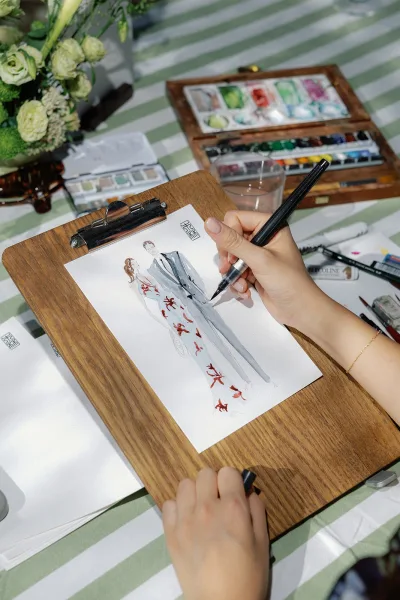 Live wedding painting in progress, a custom couple illustration with a watercolor palette on paper, set atop a striped tablecloth.