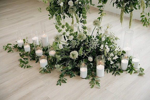 Wedding altar decor with a greenery wedding altar garland, white flowers, hanging greenery, and pillar candles in glass on a white wall