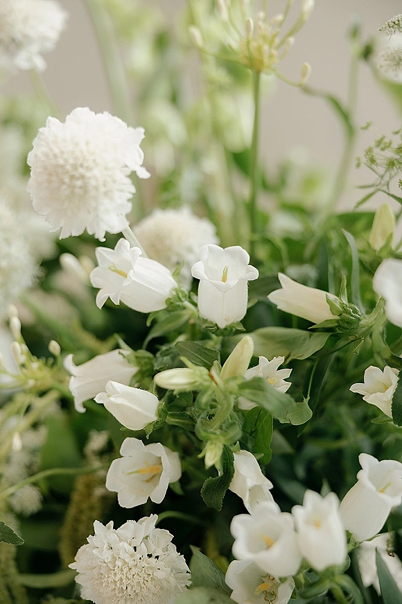 Wedding florals with white wedding flowers and soft greenery, airy stems and buds against a neutral backdrop with blurred foliage