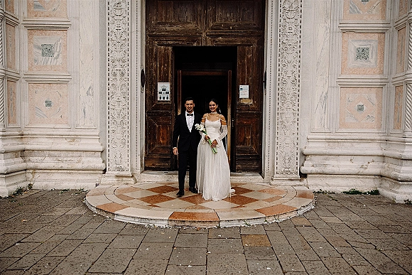 Couple portrait of bride and groom portrait on stone steps at an ornate doorway, veil and off-the-shoulder gown with calla bouquet