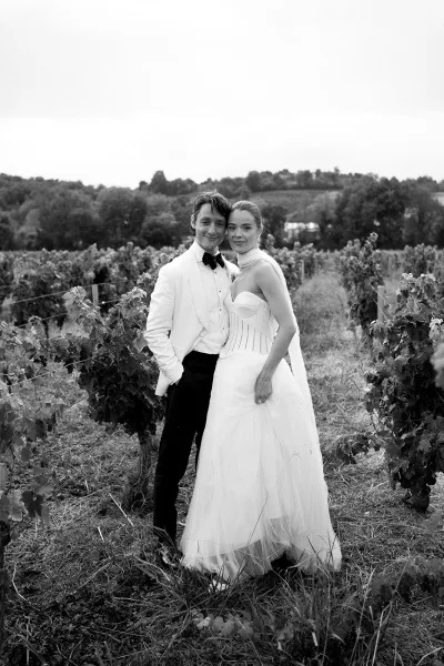 Couple portrait, black and white wedding portrait of bride in corset tulle gown and groom in white tuxedo among vineyard rows and hills