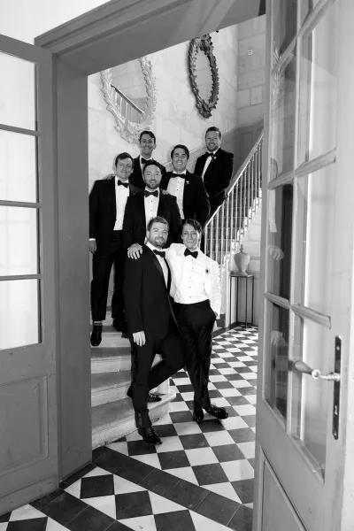 Groomsmen portrait of a groom and groomsmen in tuxedos with bow ties and boutonnieres on a stone staircase beside framed mirrors