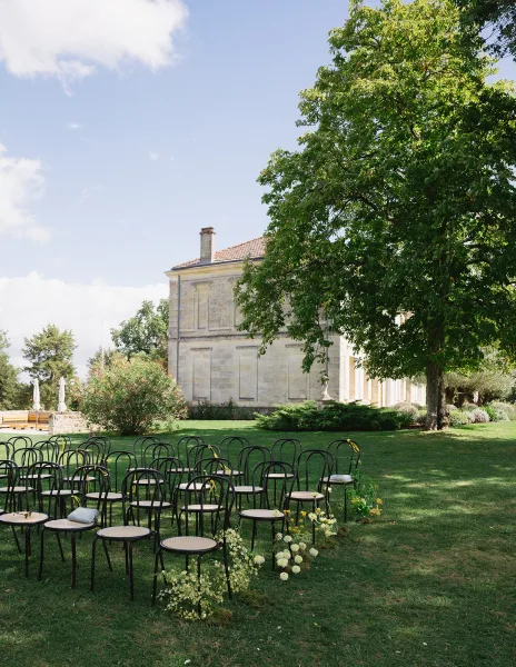 Ceremony seating with outdoor wedding ceremony chairs in neat rows, black bistro chairs with ribbon ties and ground florals on a grassy lawn under a large tree