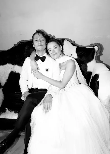 Couple portrait, black and white wedding portrait of bride hugging groom on an upholstered settee against a plain wall and wood floor