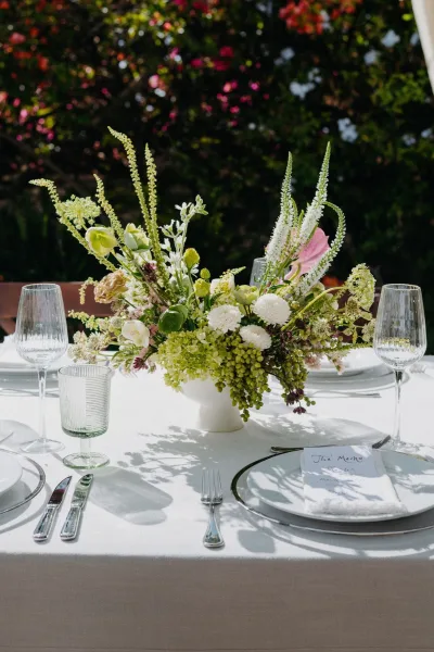 Wedding centerpiece, a green and white centerpiece arranged asymmetrically in a compote vase, set against garden greenery.