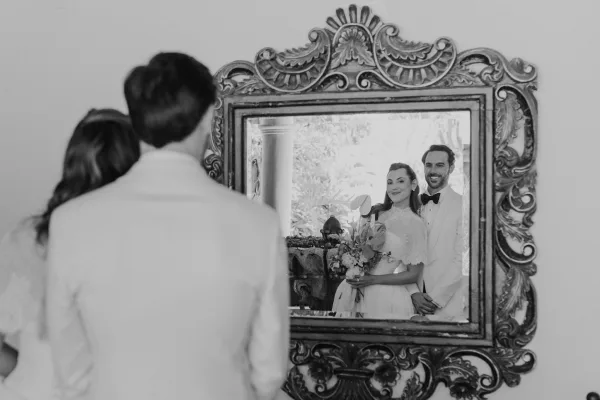 Couple portrait, a mirror wedding photo reflected in an ornate mirror, groom standing behind the smiling bride in a timeless, classic pose.