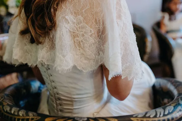 Bridal gown detail with a lace bridal cape draped over the back, highlighting delicate corset lacing.