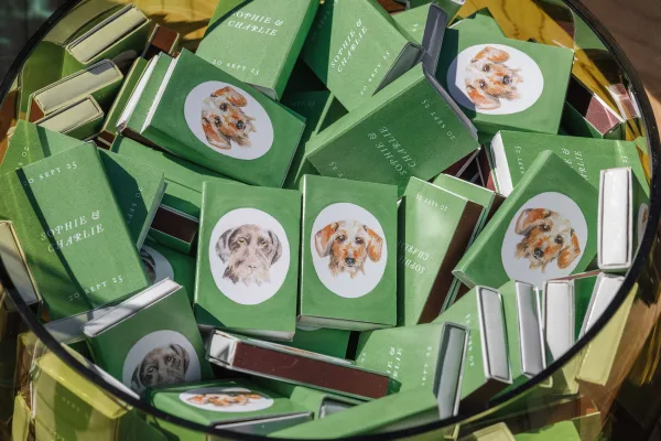 Wedding matchboxes with custom wedding matchboxes labels, pet portrait stickers, and foil-stamped text in a glass bowl on gold surface