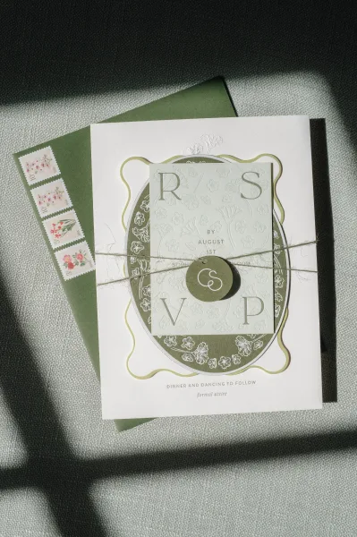 Wedding invitation suite with green wedding invitations, twine and wax seal sticker, floral postage stamps on textured fabric in soft shadows