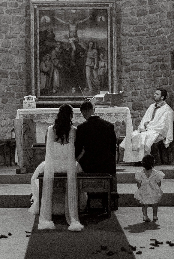 Wedding ceremony with bride and groom kneeling at the church wedding ceremony altar, long veil trailing on aisle runner with flower petals