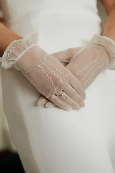 Bridal gloves in sheer bridal gloves style with ruffled lace cuffs, showing engagement and wedding rings against a neutral backdrop