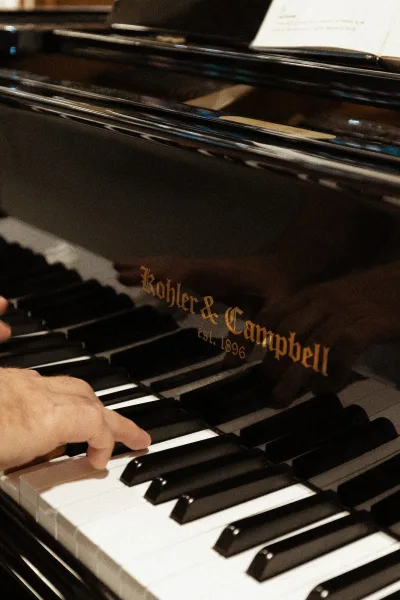 Wedding live music by a wedding pianist, hands playing piano keys on a black grand piano with sheet music in an indoor venue