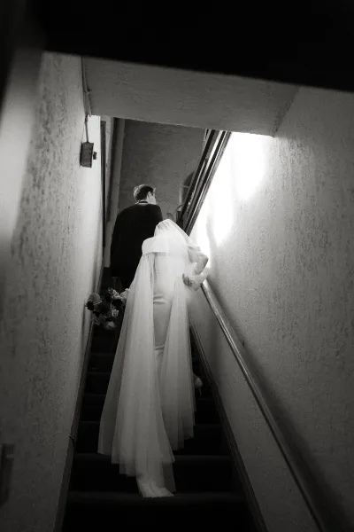 Wedding couple portrait in a black and white wedding portrait, bride and groom walking up a staircase, veil train and bouquet in hand under overhead light