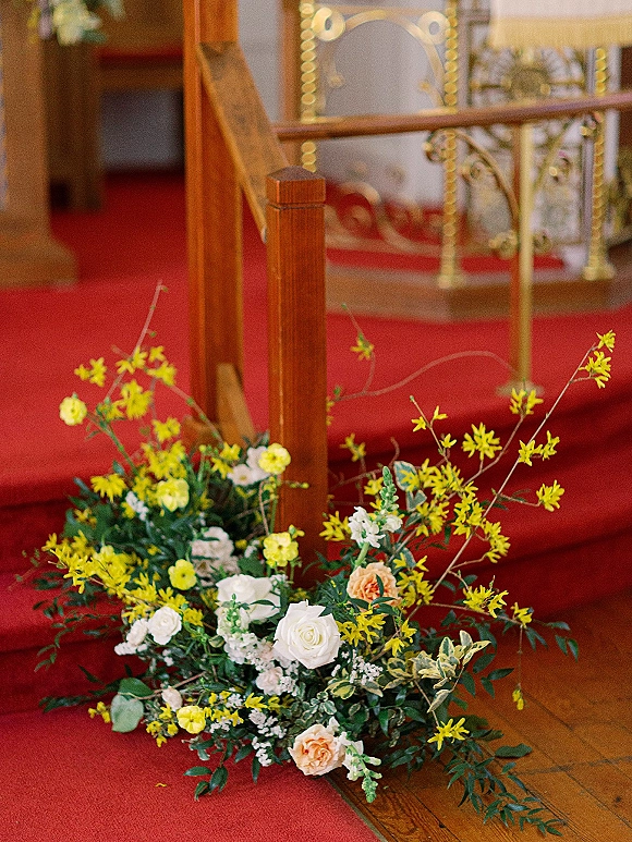 Wedding aisle flowers and aisle floral arrangement with white roses and yellow blooms along a red carpet church aisle by a wooden banister