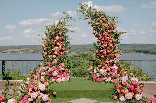 Wedding ceremony backdrop with floral ceremony arch pillars of roses, hydrangeas, and greenery framing an aisle on a lakeview terrace patio