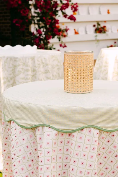Wedding lounge decor with wedding lounge seating, a woven candle holder on a patterned ottoman and upholstered stools by white siding with a flowering vine