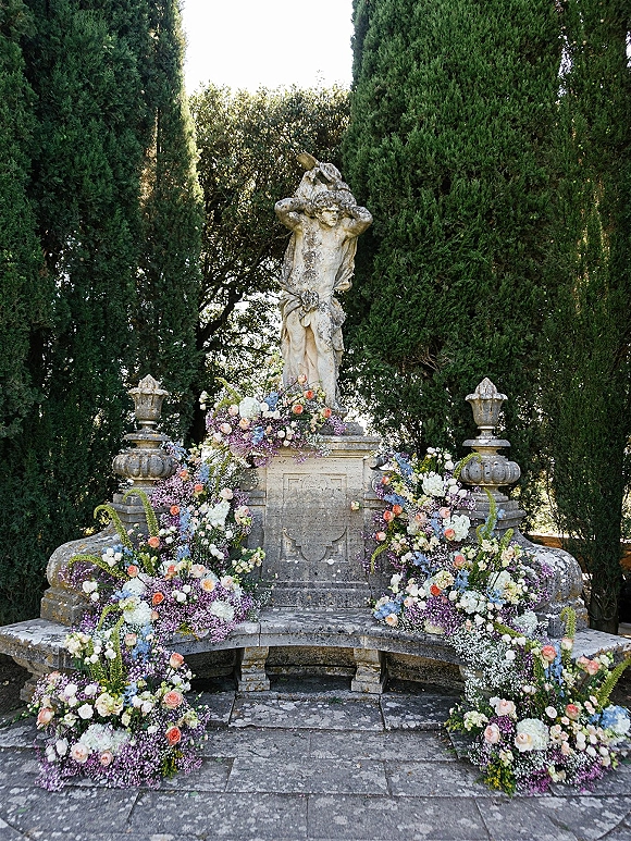 Ceremony altar decor with floral ceremony backdrop on a stone statue and bench, roses and hydrangeas on a garden patio under evergreens