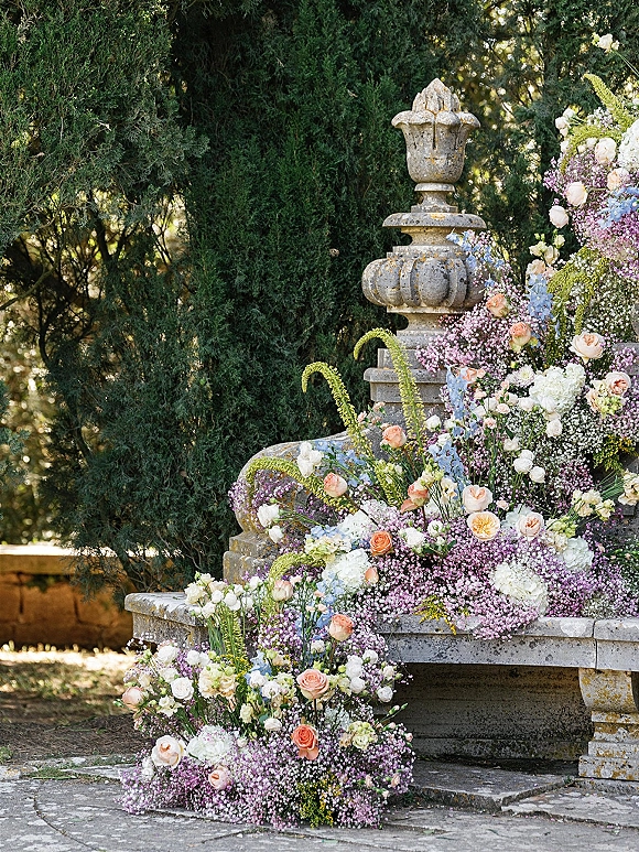 Wedding ceremony flowers in a stone urn and ground installation of roses, baby's breath, hydrangeas, and greenery on garden paving