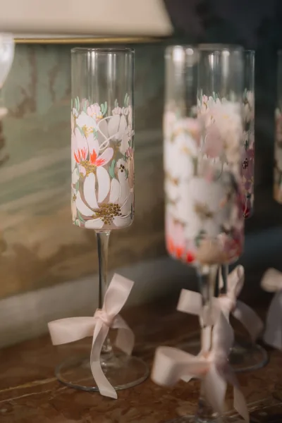 Wedding toasting flutes, hand painted champagne glasses adorned with hand-painted florals, resting on a marble tabletop.
