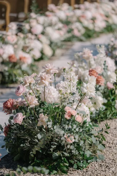 Ceremony aisle flowers serve as floral aisle markers, low clusters of roses lining a stone path between rows of ceremony chairs.