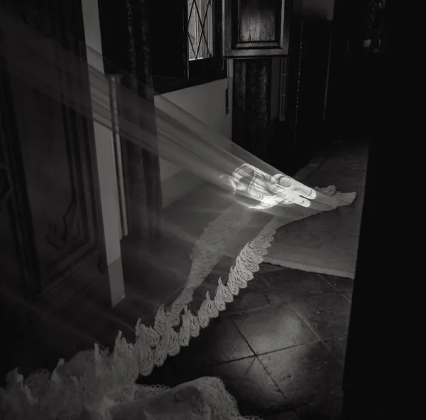 Bridal veil with a long veil train and a scalloped edge sweeping across a tile-floored hallway by a wooden door and window.