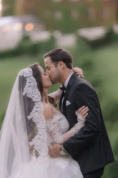 Wedding kiss portrait, a tender couple portrait of a bride in a lace veil kissing her groom amid lush garden greenery and hedges.