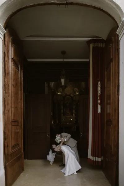 Wedding couple portrait in a wedding dip kiss, bride in satin dress and veil holding bouquet as groom leans in by arched wooden doors