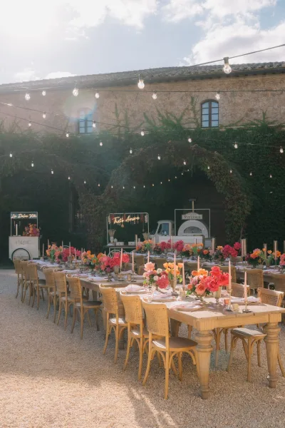 Reception tablescape showcasing outdoor reception decor beneath warm string lights in a gravel courtyard with an ivy-covered wall backdrop.