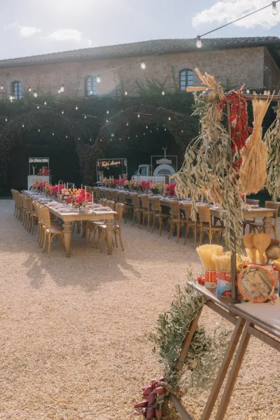 Outdoor reception decor for an al fresco wedding reception with string lights in a gravel courtyard beside an ivy-covered stone building with arches.