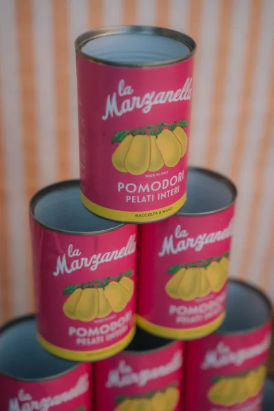 Tomato can display arranged as colorful food can decor, featuring colorful labels against a striped fabric backdrop