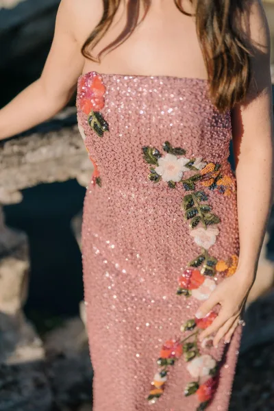 Sequin dress close-up of a strapless sequin gown with floral embroidery, shimmering against a stone and water backdrop.