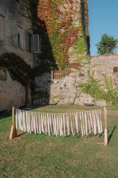 Ribbon backdrop on a wooden stand for a DIY wedding backdrop, layered ribbons flutter before a stone wall with ivy under a blue sky.