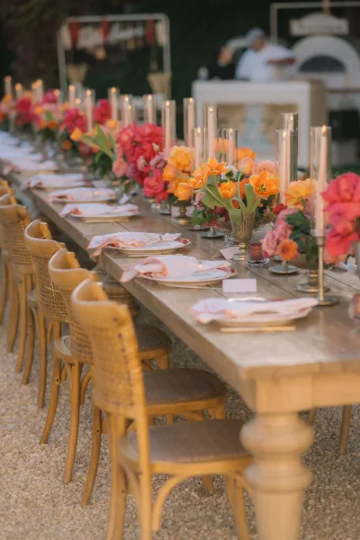 Reception tablescape on a long reception table with floral centerpieces, set on gravel amid lush garden greenery for an al fresco feel.