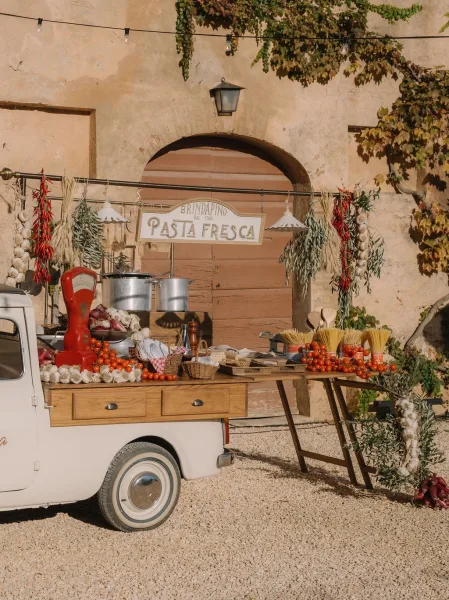 Pasta bar setup as a wedding food station featuring a hand-cranked pasta maker, set against an ivy-clad stucco wall in a gravel courtyard.