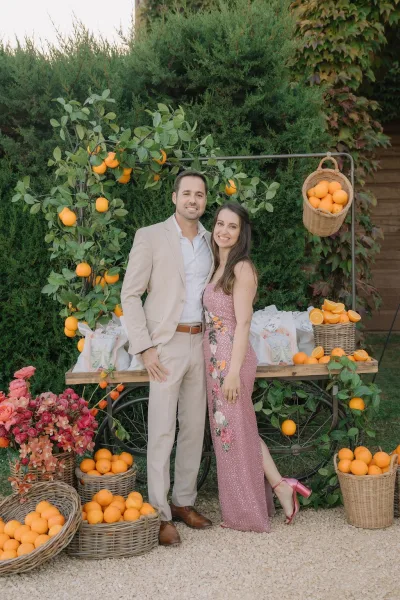 Couple portrait against a citrus backdrop, framed by a citrus garland, the pair standing by ivy-clad garden hedges.