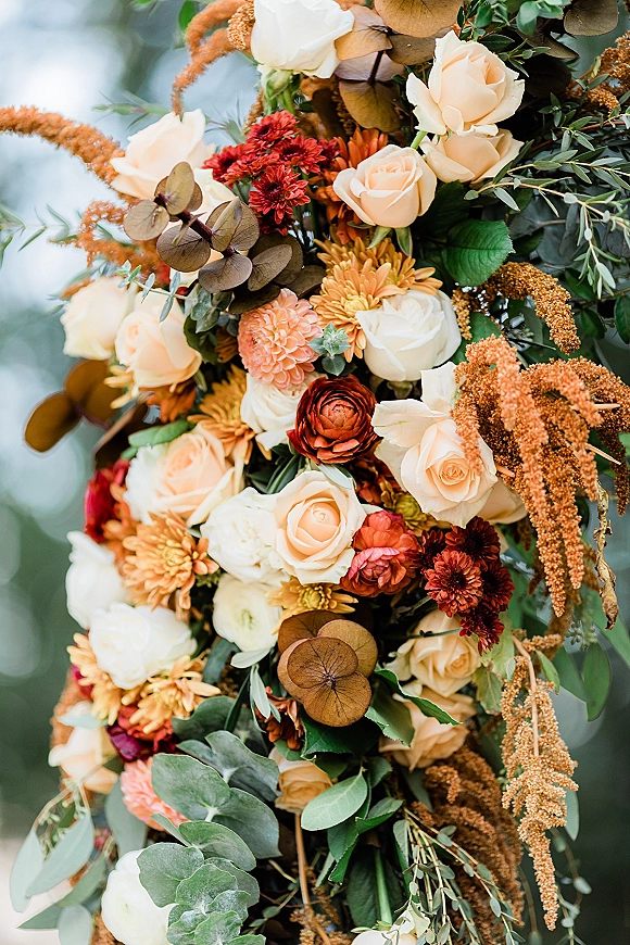 Wedding floral arrangement of autumn wedding flowers with cream roses, rust ranunculus, chrysanthemums and eucalyptus against blurred greenery