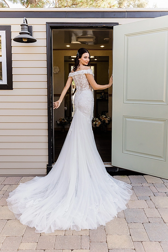 Bridal portrait of a bride in an off the shoulder wedding dress, looking over her shoulder in an open doorway with long tulle train