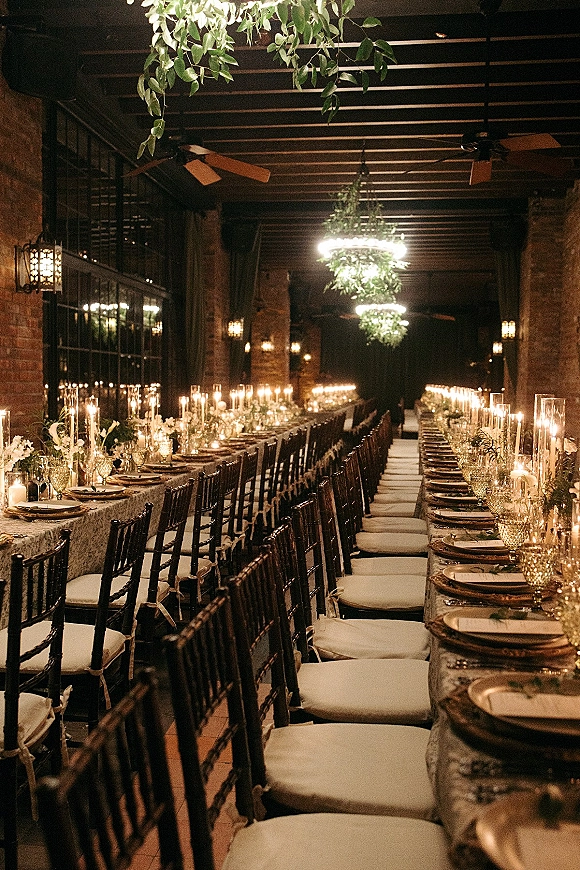 Reception tablescape with long banquet table wedding styling, taper candles in glass hurricanes and greenery garlands in a brick hall with arched windows