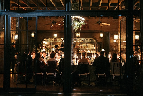 Wedding reception dinner with candlelit wedding reception tables, tall cylinder candles and floral centerpieces in a brick-walled bar lounge