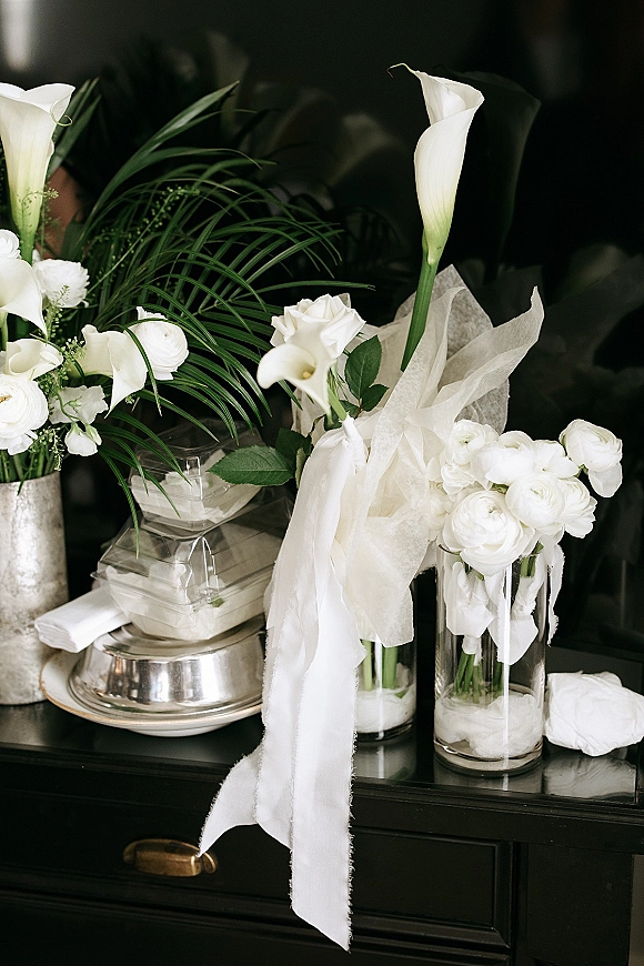 Wedding bouquet with white calla lilies and roses, wrapped in tissue and ribbon, arranged on a dresser in a dark interior
