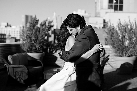 Couple portrait in a black and white wedding portrait style, bride in wedding dress and groom in suit jacket embracing on a rooftop terrace skyline