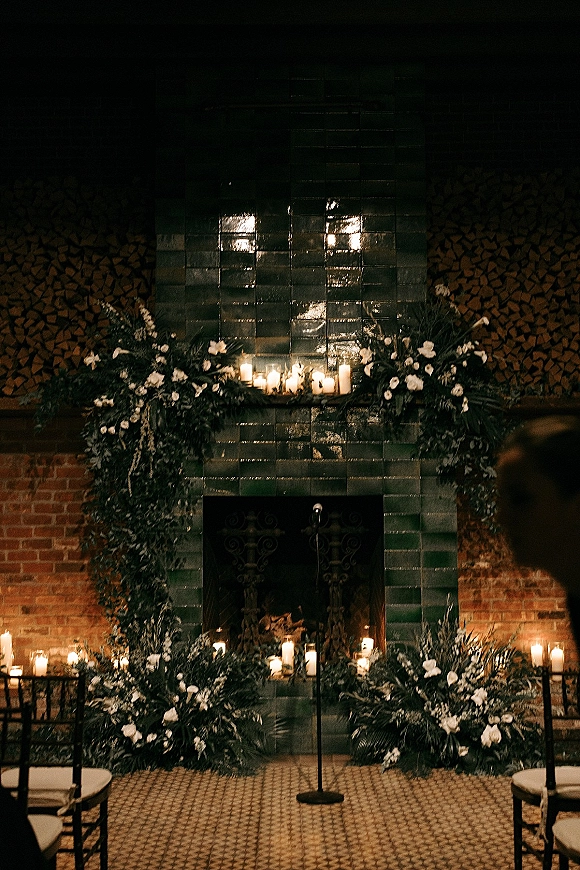 Wedding ceremony backdrop with fireplace wedding ceremony decor, floral garland and pillar candles on a tiled mantel with chairs facing forward