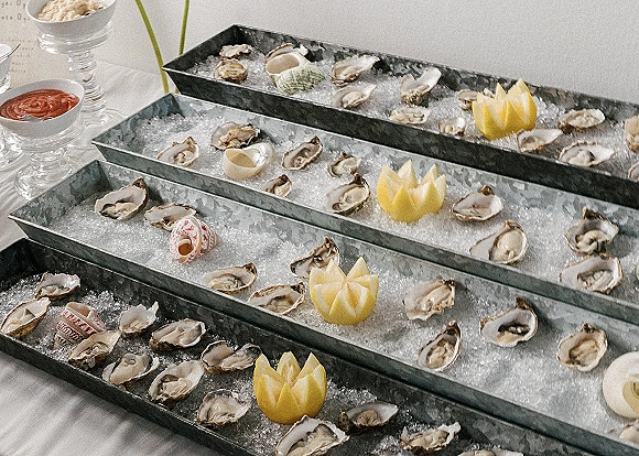 Oyster bar with oysters on the half shell over crushed ice in galvanized trays, garnished with lemon, with cocktail sauce on a white tablecloth