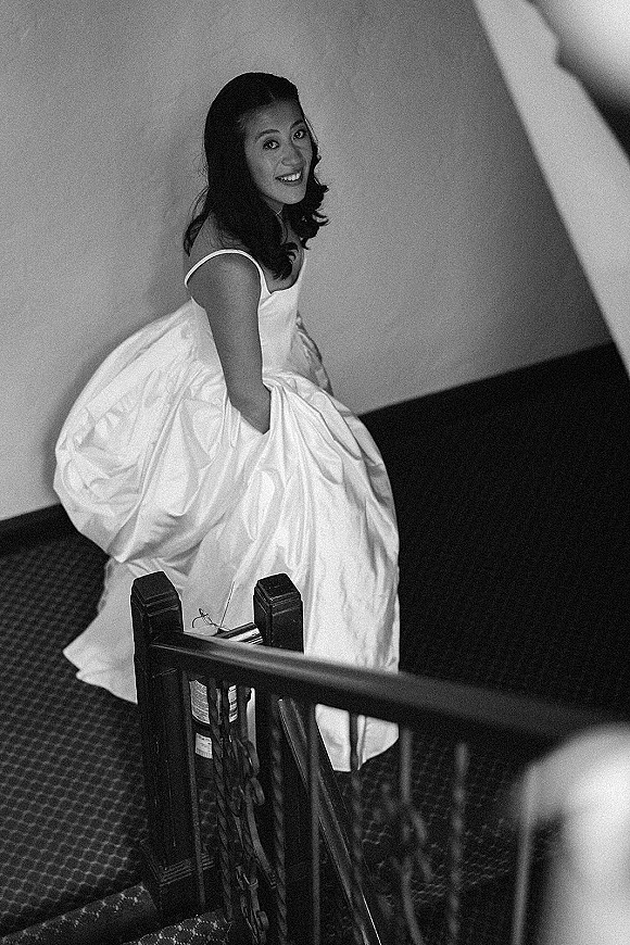 Bridal portrait of a bride in a spaghetti strap wedding dress smiling and looking back on a staircase with railing and carpeted floor
