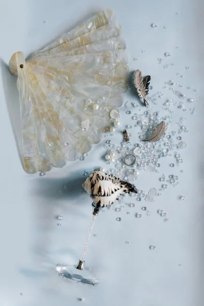 Bridal fan, a mother of pearl fan adorned with pearls, resting on a soft light blue fabric backdrop