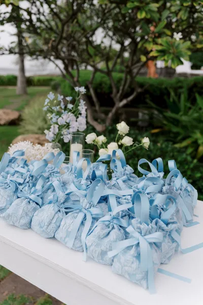 Wedding favor bags arranged as drawstring favor pouches with ribbons, styled in a garden setting among trees and greenery.
