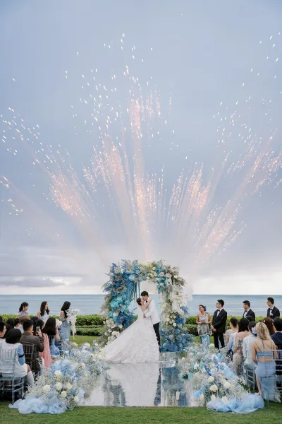 Ceremony kiss moment as the wedding first kiss unfolds beneath a circular floral arch, framed by the ocean horizon and open sky.