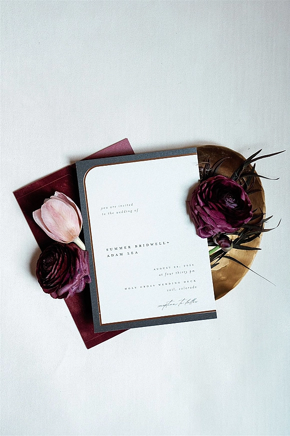 Invitation suite wedding invitation flat lay with card and envelope, floral accents, and a gold dish on a clean white backdrop